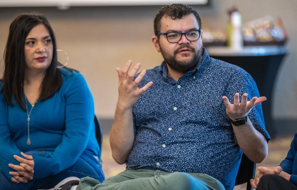 Man sitting in a chair next to a woman and talking with his hands.