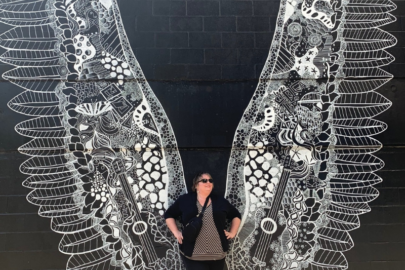 Jen Wilkins in front of a black and white mural of angel wings