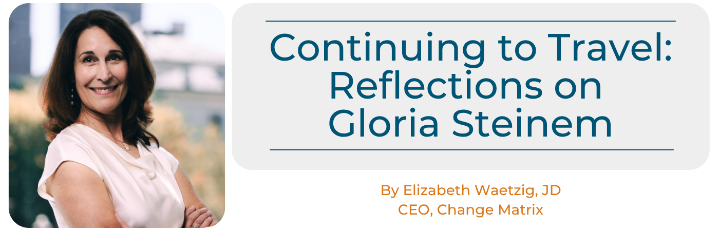 A header graphic for a blog article featuring a portrait photo on the left of a smiling woman with shoulder-length brown hair, wearing a light pink blouse, standing outdoors with her arms crossed. To the right, a light gray rounded rectangle contains the article title in dark teal text: 'Continuing to Travel: Reflections on Gloria Steinem.' Below the title box, orange text reads 'By Elizabeth Waetzig, JD' and 'CEO, Change Matrix,' identifying the author as the CEO of Change Matrix.