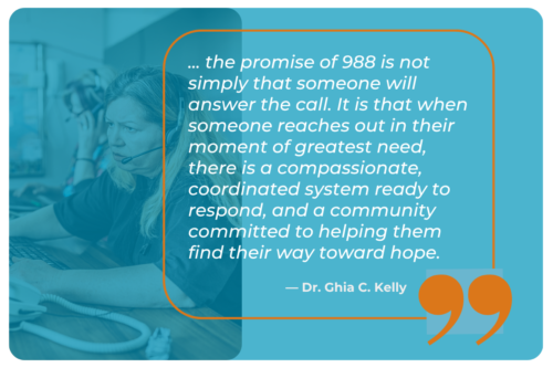 A graphic with a blue-toned background photo of a crisis line operator wearing a headset while working at a computer. Overlaid in an orange-bordered box is a quote: '... the promise of 988 is not simply that someone will answer the call. It is that when someone reaches out in their moment of greatest need, there is a compassionate, coordinated system ready to respond, and a community committed to helping them find their way toward hope.' The quote is attributed to ' - Dr. Ghia C. Kelly' and large orange quotation marks appear in the bottom right corner.
