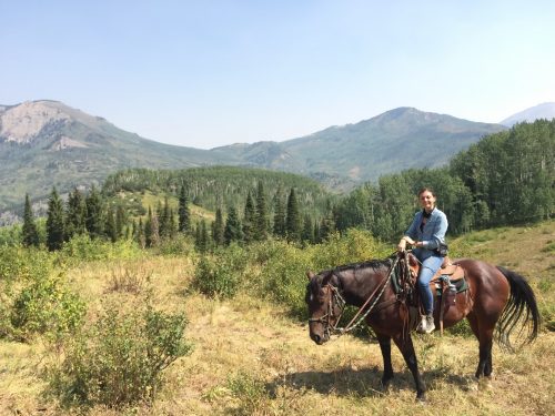 Lauren riding a horse through a meadow among the mountains