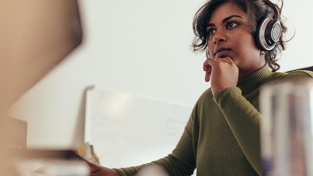 A woman with a green shirt and headphones on looking at something with a lot of thought