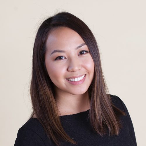 A photograph of Nancy Vang smiling in a black top and in front of a creme colored background