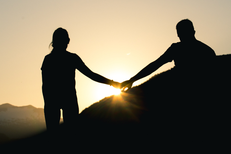 Two silhouettes of people holding hands during a sunset.