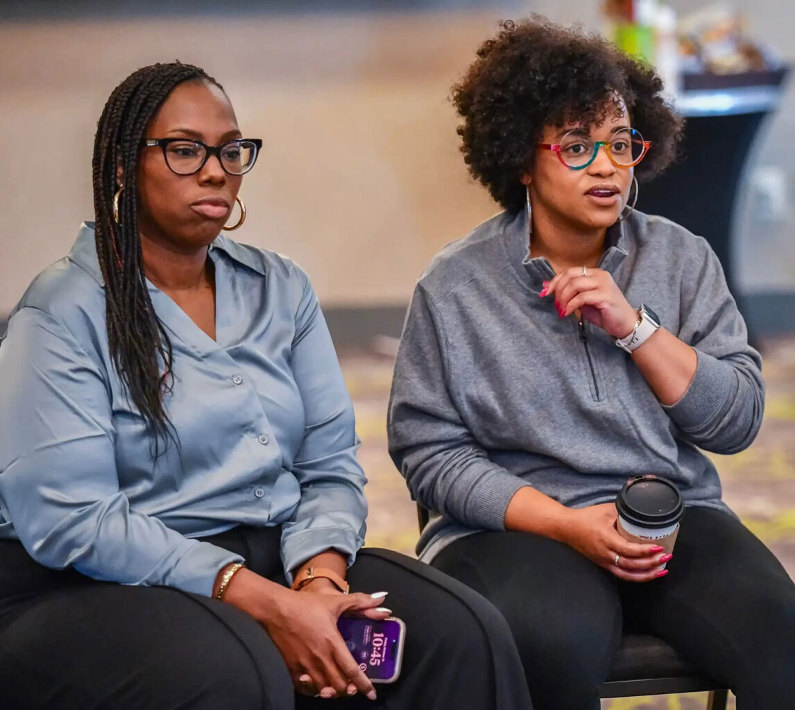 Two women at a professional work conference sitting and talking in a group setting.
