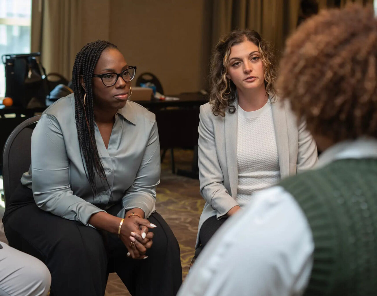 Employees at a work conference sitting, listening, and talking to one another.