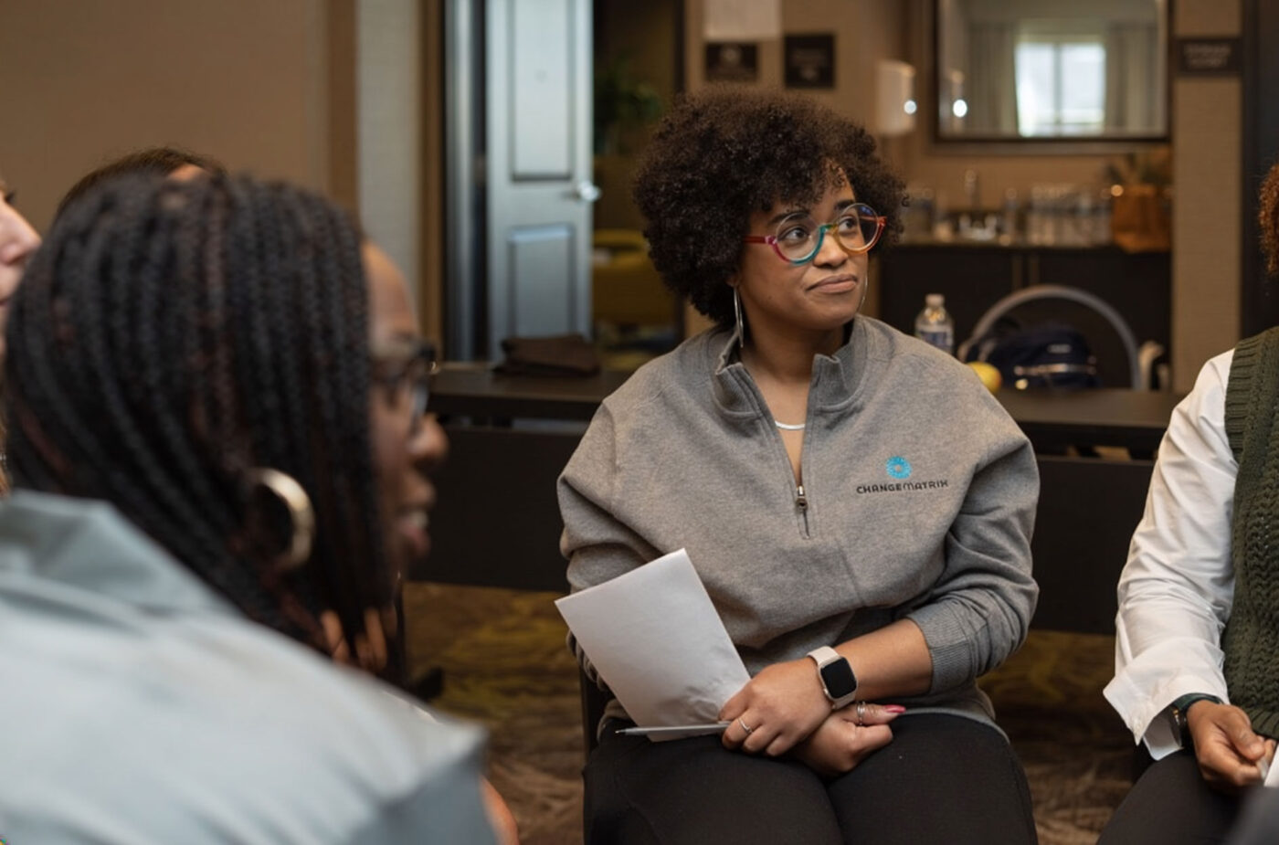Group of women sitting in chairs in a circle listening to someone speak not in the photograph. Looks like they are at a professional work conference.